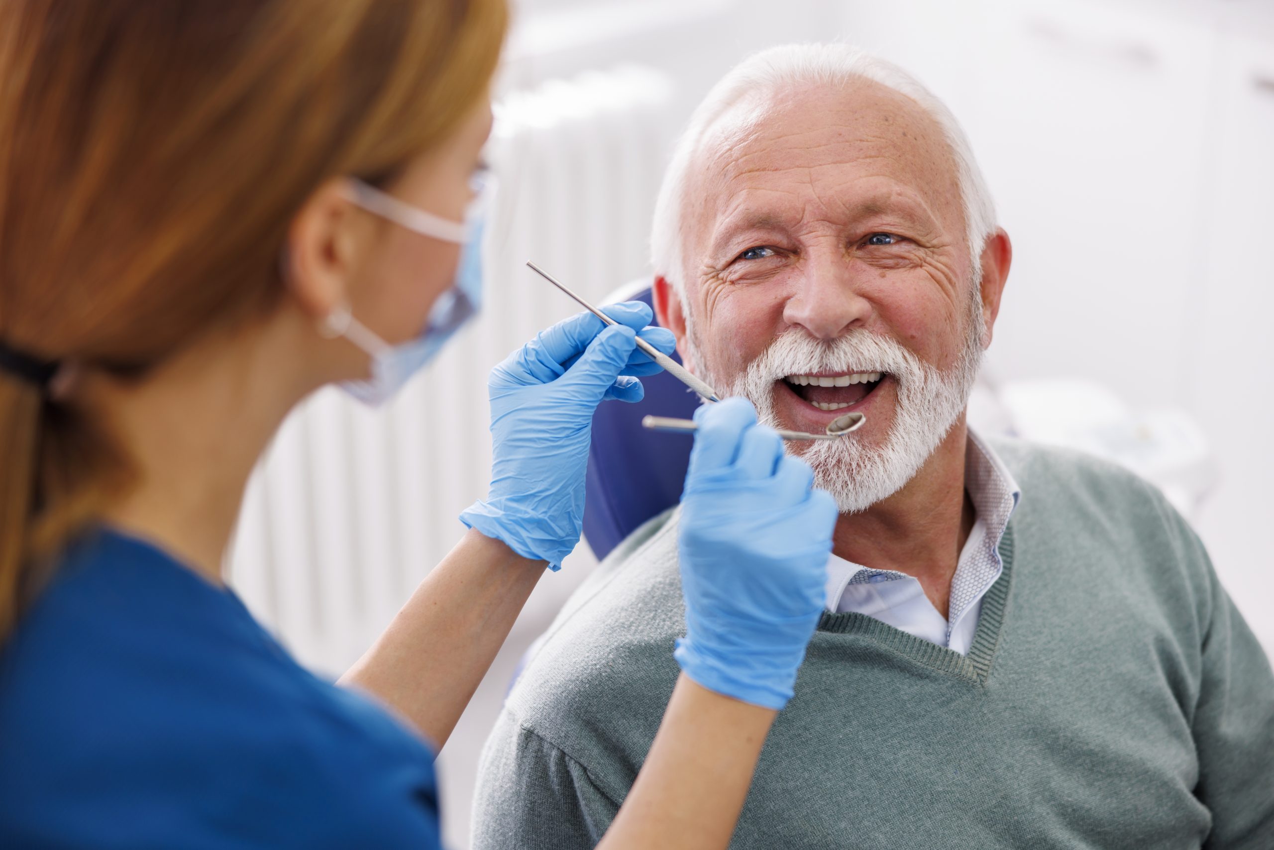 Doctor checking up patient's teeth at dentist office; senior man at dental checkup